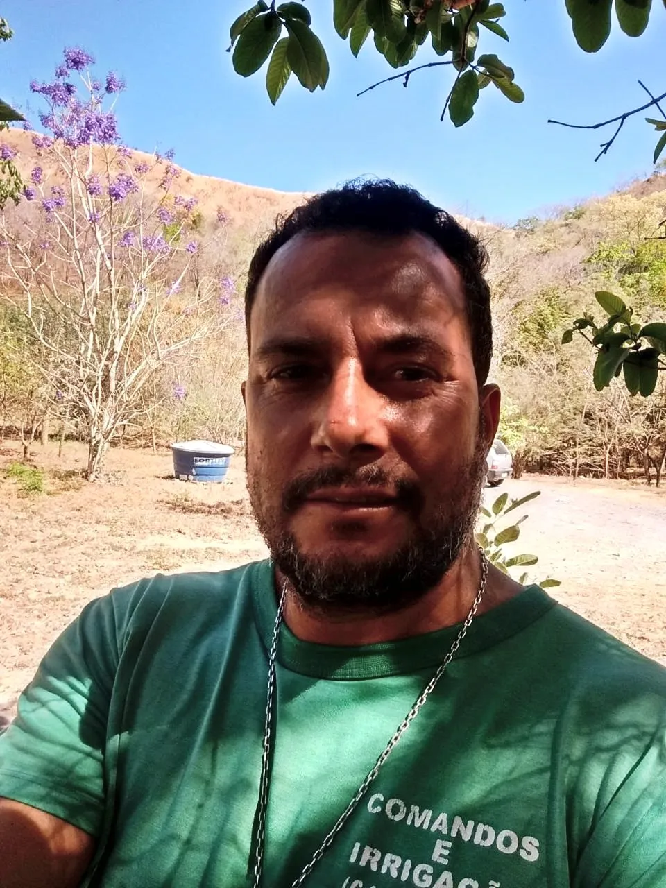 Lindomário Rodrigues, de camiseta da Comandos & Irrigação, em uma área rural com reservatório de água ao fundo